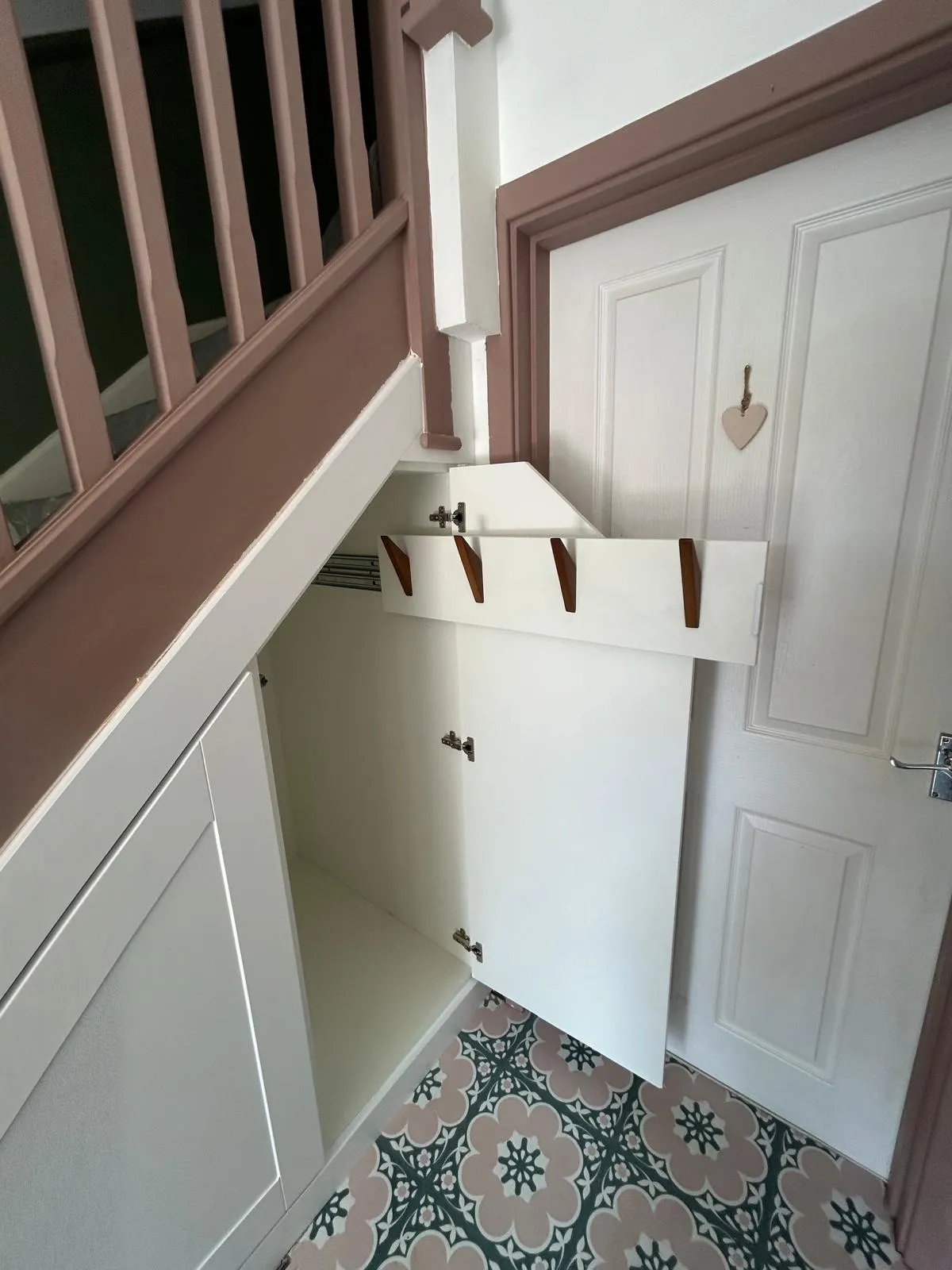 A hinged under stairs cupboard door open, with a pull out coat rail extended