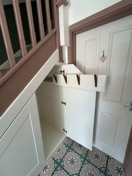 A pull out coat rack extended from an under stairs cupboard in a period hall